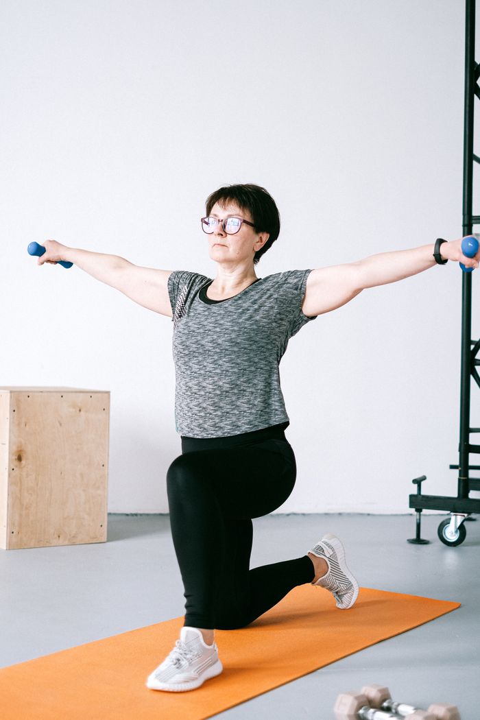 Senior woman practicing fitness indoors with dumbbells on an exercise mat.